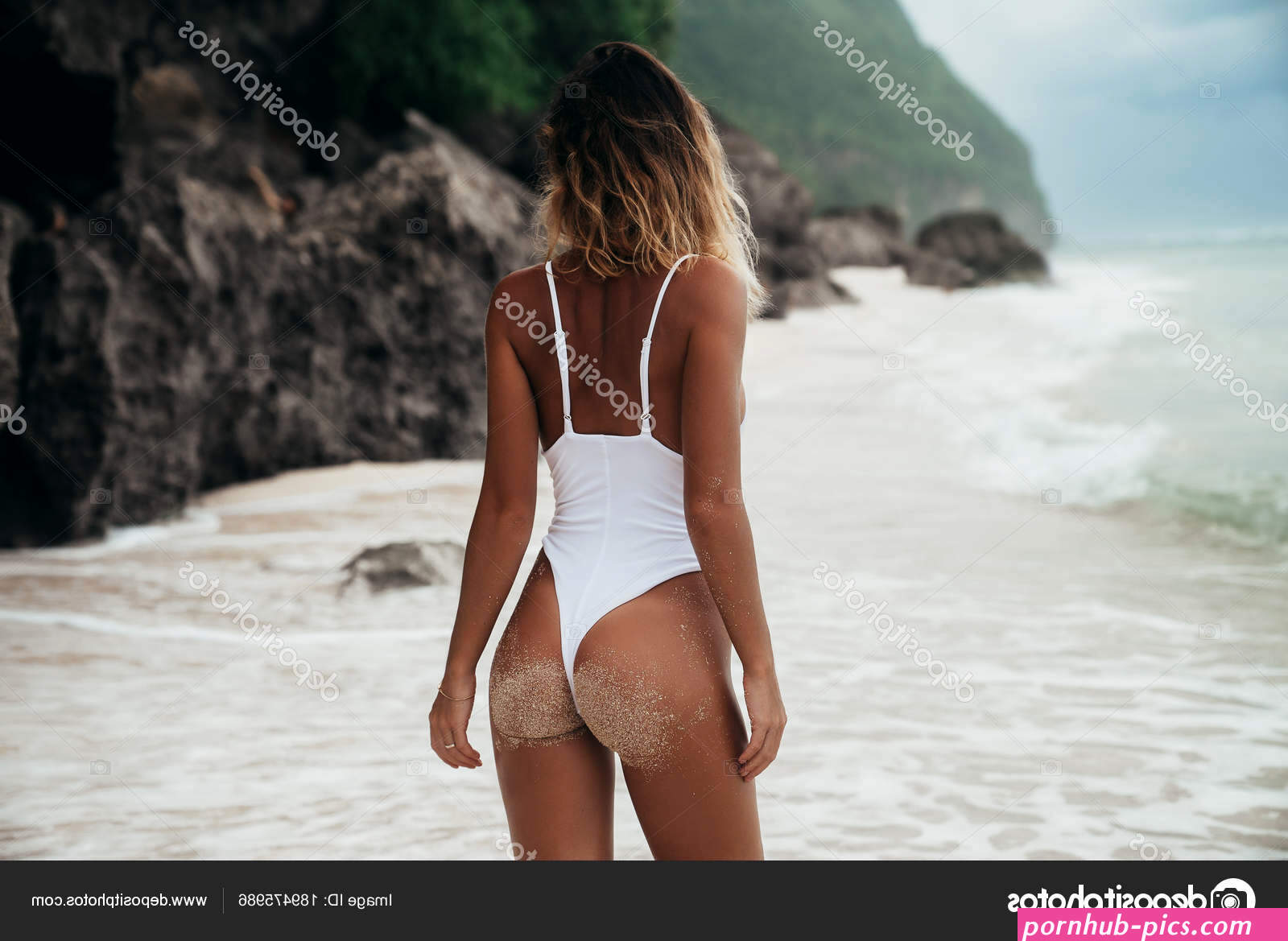 Back view sexy girl in white swimsuit with perfect sporty body, nice booty and curly hairs relaxing at the beach. Pretty woman traveller taking sunbathes. Concept of fitness model in swimwear Stock