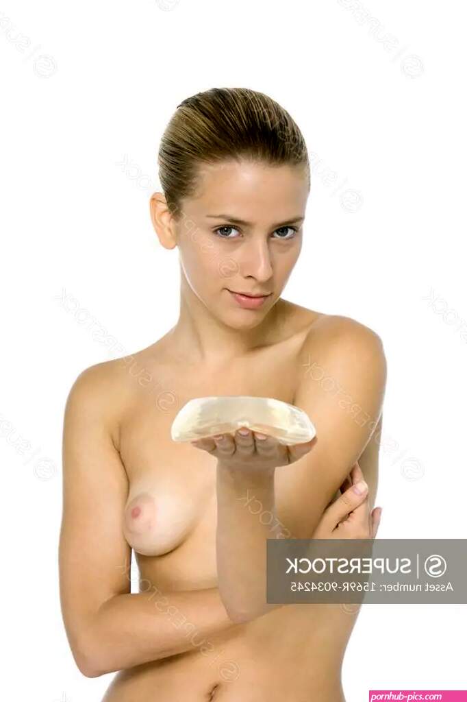 Nude woman holding breast implant looking at camera