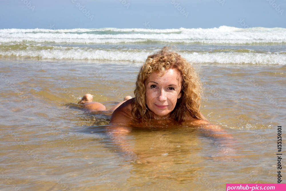 Beautiful blond european girl lying on sandy beach nude Stock