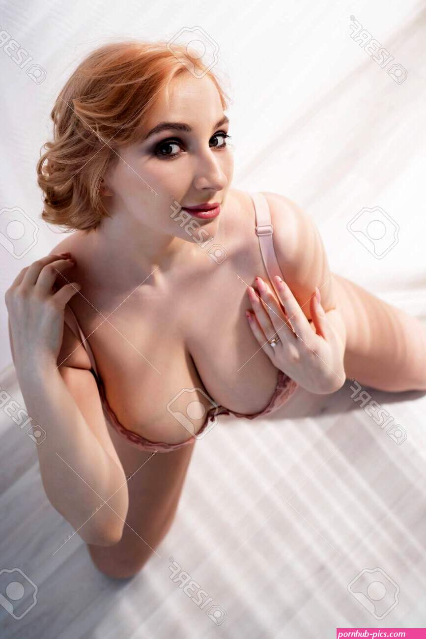 A Beautiful Young Woman With Very Large Natural Breasts Sits On Her Knees On The Light Floor. A Girl In Pink Lace Shows A Beautiful Figure. Top View. Huge Female Boobs. Stock
