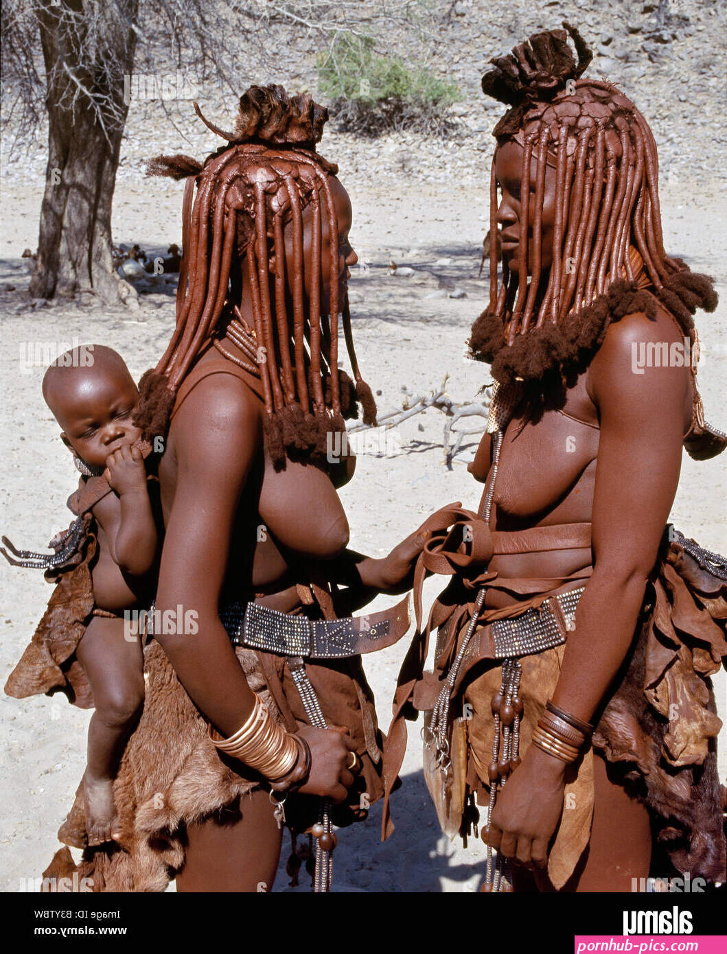 Namibia Kaokoland Empembe. Two Himba woman pause for a chat one of them with her baby in a leather baby-carrier on her back Stock Photo