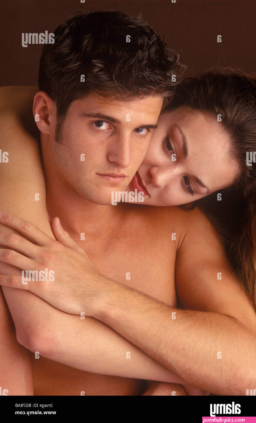 young couple naked to the waist with the woman cuddling the man and the man looking slightly irritated Stock Photo