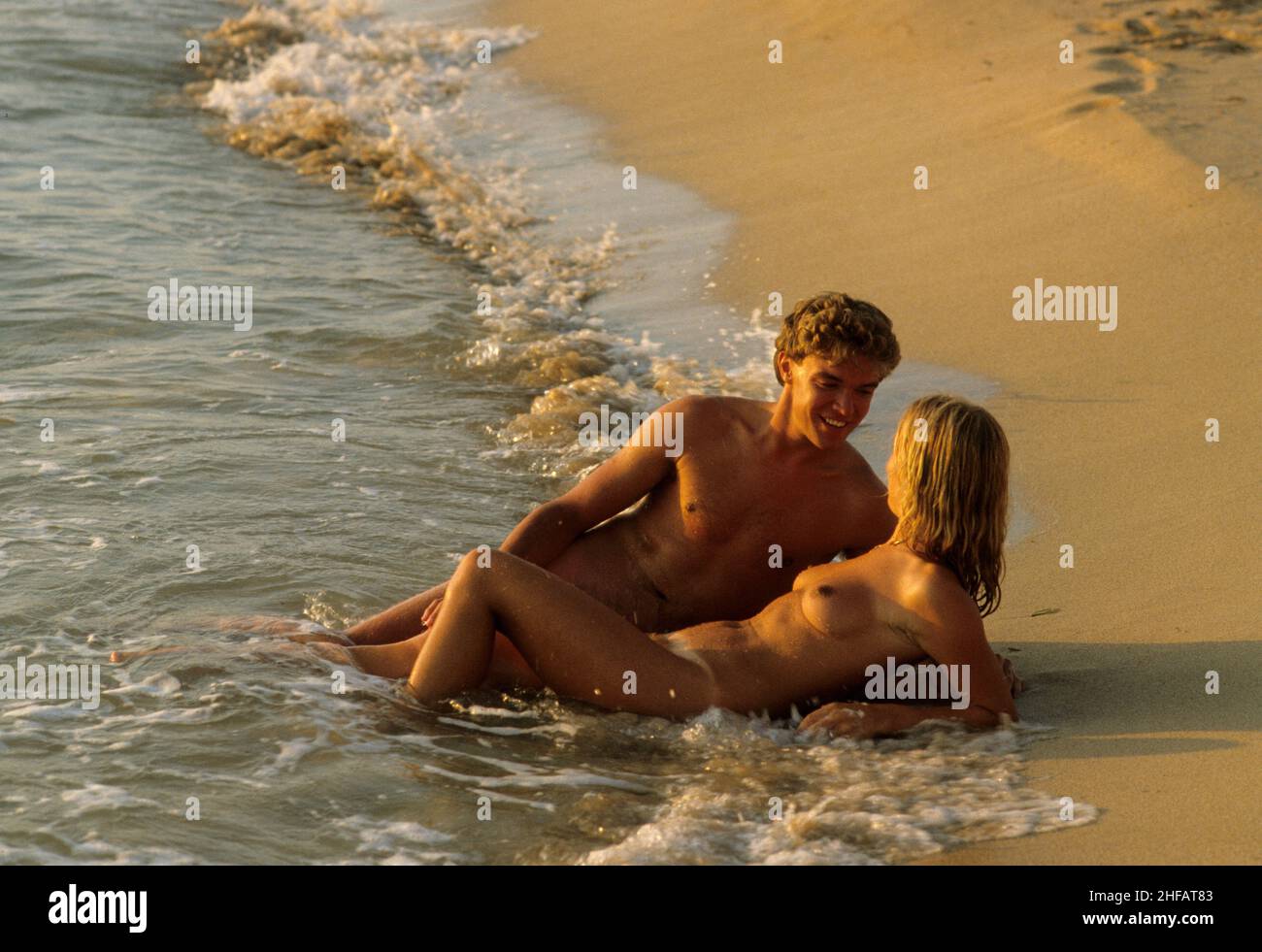 young couple embrace nude lovers on beach sunset topless naturist Stock Photo