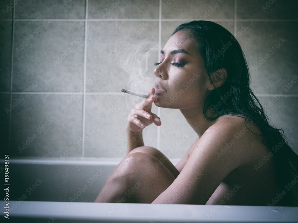 Nude woman smoking cigarette in the bath room