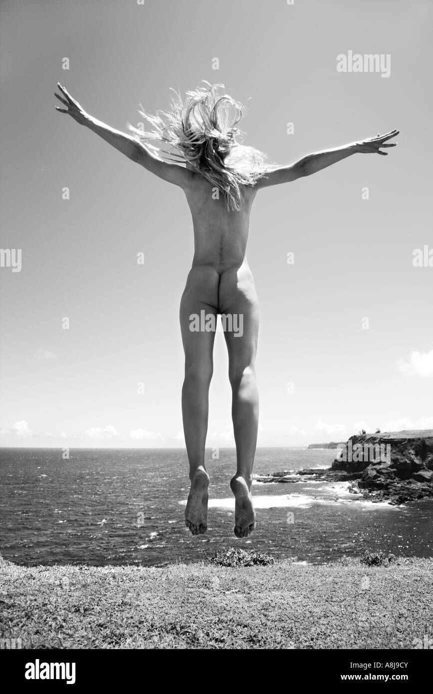 Young adult nude Caucasian woman jumping in air near cliff at Maui coast Stock Photo