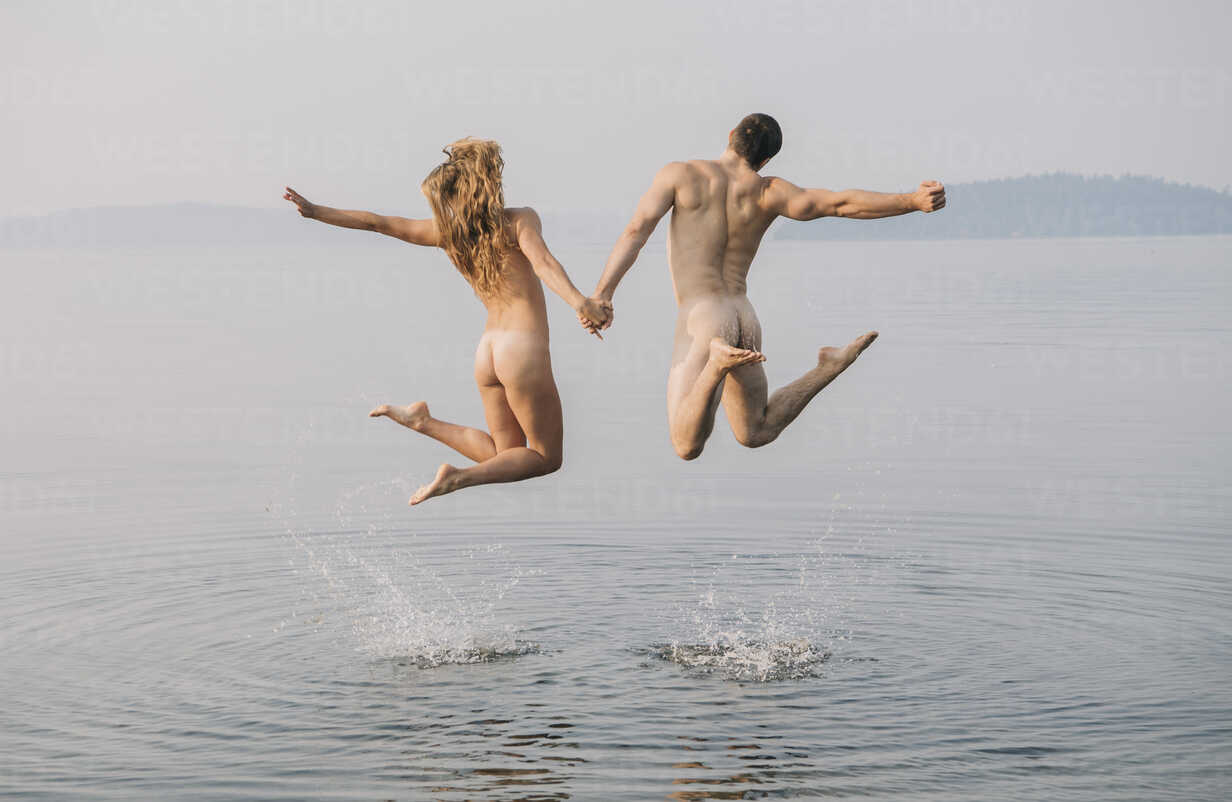 Rear view of nude couple in water jumping in mid air stock photo