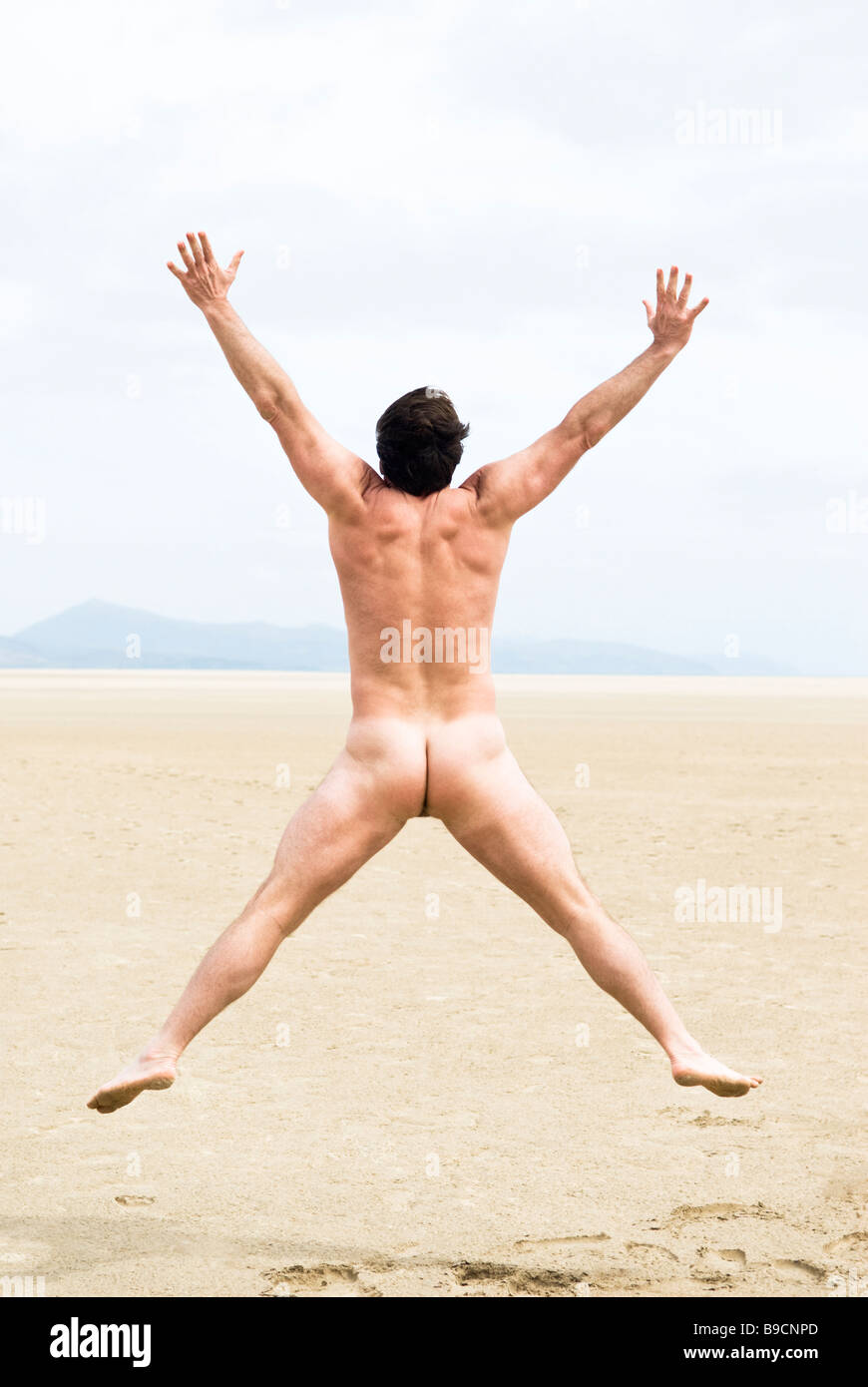 A naked fit forties man is jumping for joy on a beautiful sandy beach on the island of Fuerteventura Stock Photo