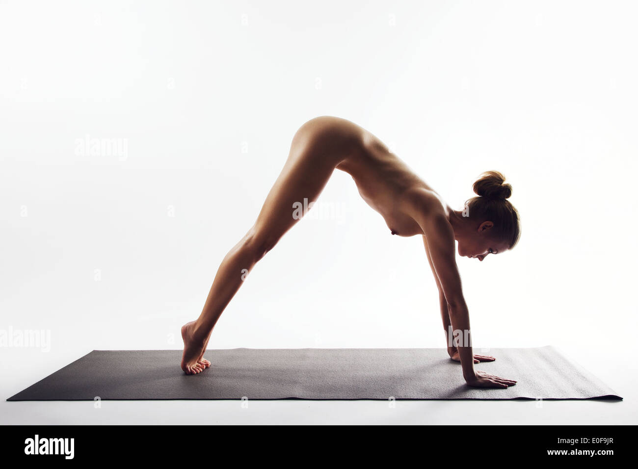 Naked young women performing stretching exercise on white background. Yoga forward bend pose demonstrated by nude female model Stock Photo