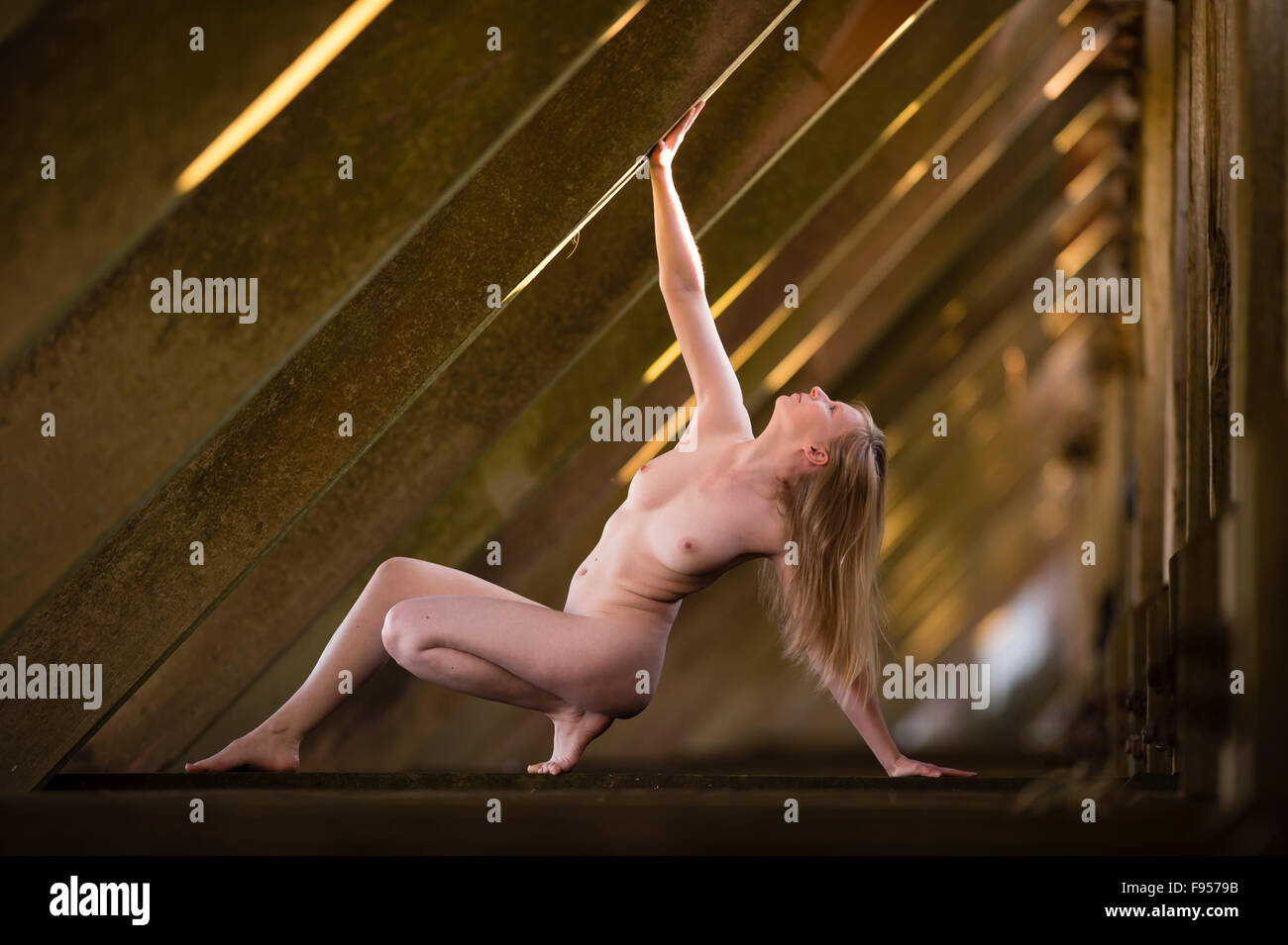 Healthy lifestyle and well-being: A naked nude young blonde woman exercising keeping fit balancing stretching Stock Photo