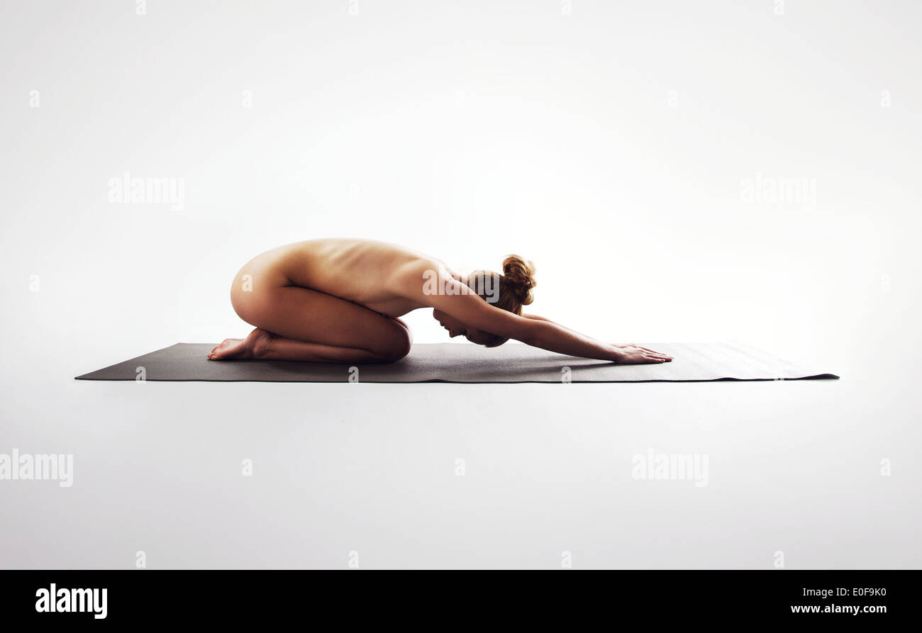 Nude young woman stretching on exercise mat. Naked caucasian female model performing yoga on white background with copy space Stock Photo