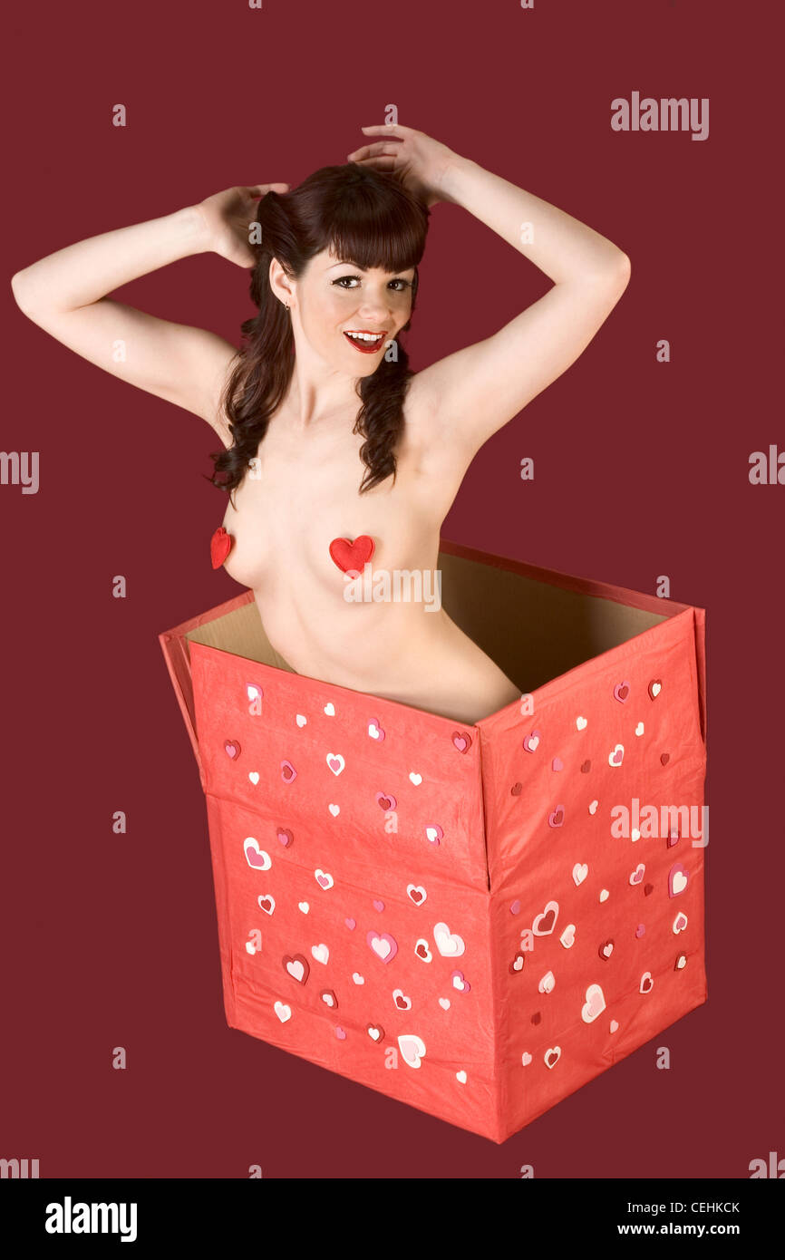 Sensual pinup brunette girl with her boobs covered by heart shaped pasties sitting in huge Valentine Day gift box Stock Photo