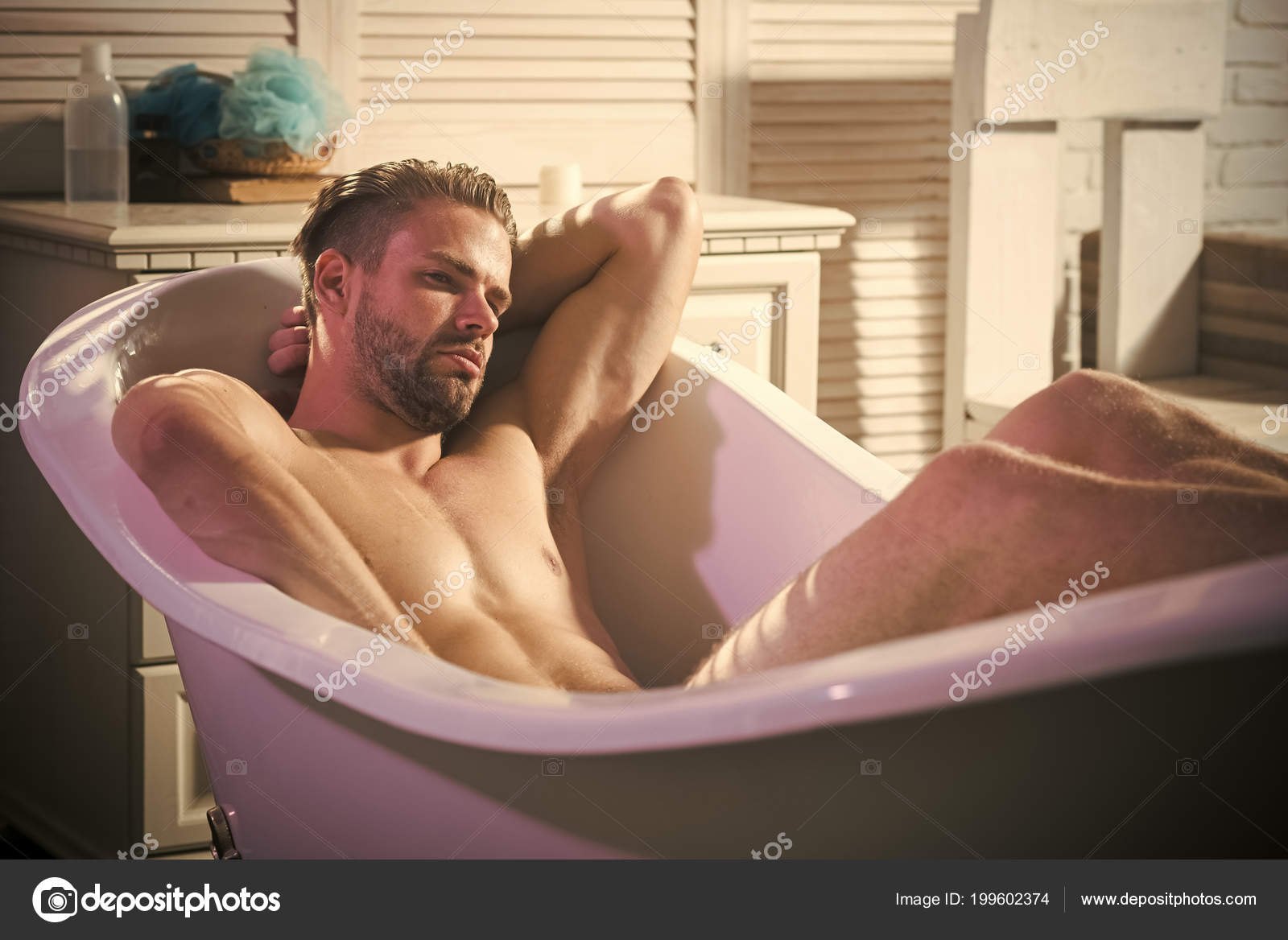 Man is betrokken bij masturbatie in de badkamer. Man met mooie blote lichaam zit in witte badkuip Stockfoto 199602374