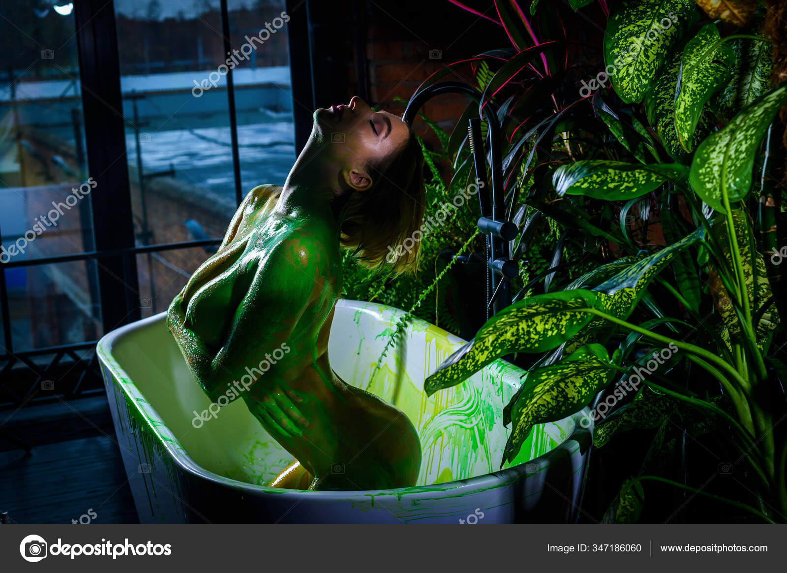 Beautiful european woman with very big breasts takes a bath. green paint flows down the naked body of a girl in the bathroom. Creative body art. Stock Photo inside-studio 347186060