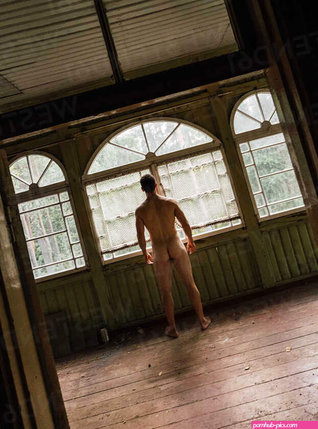 Back view of naked man standing at window of abandoned house stock photo