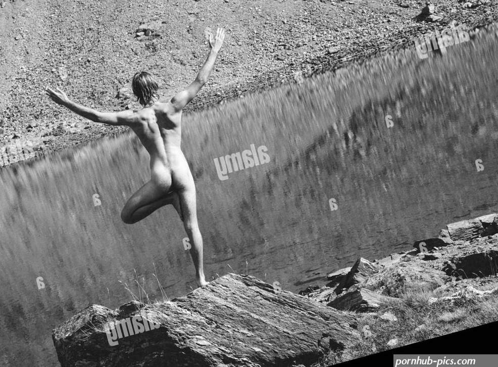 Naked yogi man does yoga asana pose in stony mountain landscape with lake reflections Stock Photo