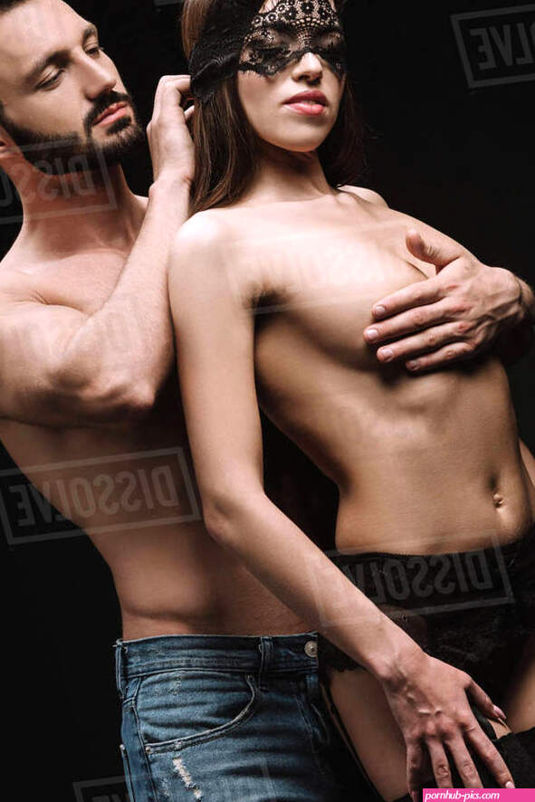 Handsome boyfriend hugging sexy nude girlfriend in lace mask isolated on black