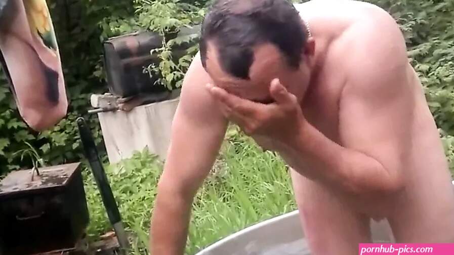 Naked old man rolls around in outside bath tub.