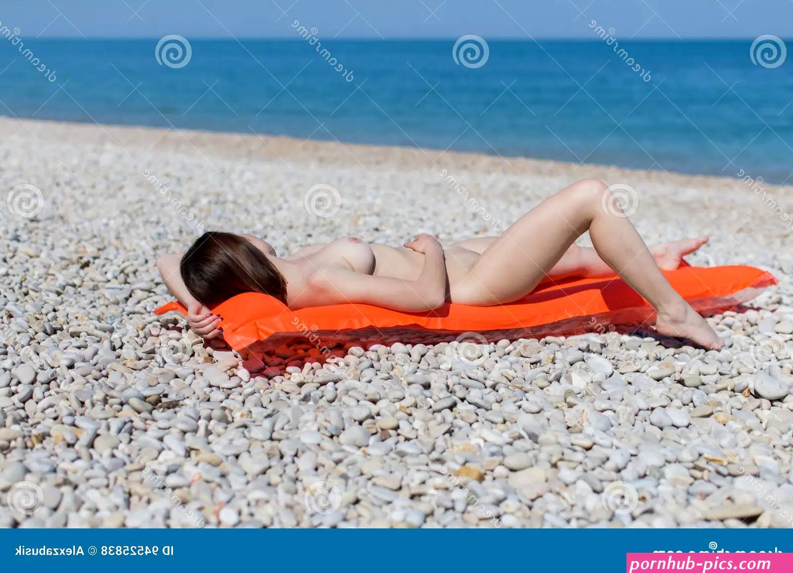 Young Woman Sunbathes on Pebble Seashore Stock Photo